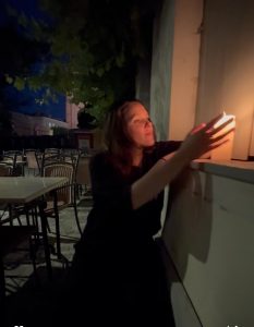 Isabell Rahms in schwarzer Kleidung mit Kerze am Eingang der Rotekopfgasse in Mainz, im Hintergrund die beleuchtete Silhouette des Mainzer Doms bei Nacht.