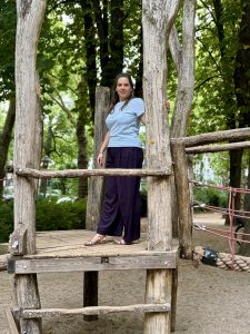 Isabell Rahms auf dem Klettergerüst am Spielplatz Gartenfeldplatz in der Mainzer Neustadt, umgeben von hohen grünen Bäumen.