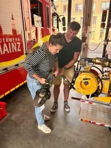 Isabell Rahms mit Maik Bittner vom Förderverein der Berufsfeuerwehr Mainz mit hydraulischer Rettungsschere zwischen zwei Feuerwehrautos