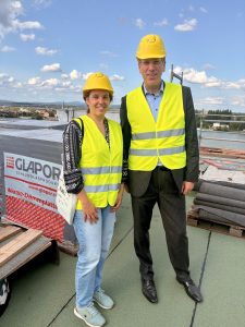 Stadträtin Isabell Rahms und Dezernent Ludwig Holle auf dem Dach der Baustelle des Mainzer Rathauses mit Blick auf den Rhein, in gelben Warnwesten und Schutzhelmen