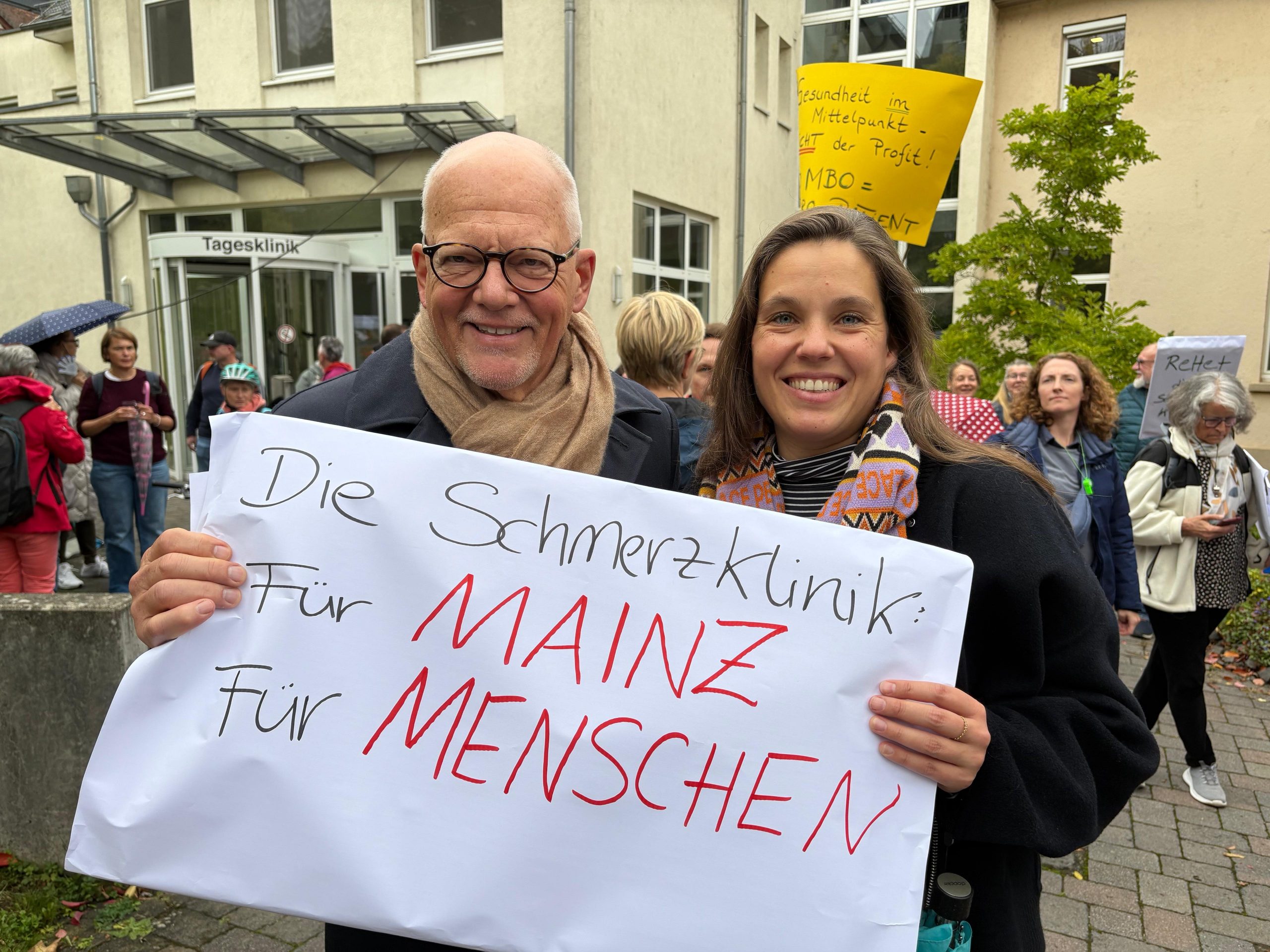 Isabell Rahms und Prof. Dr. Hans-Raimund Casser, ehemaliger ärztlicher Direktor des Schmerz-Zentrums Mainz, halten gemeinsam ein Schild mit der Aufschrift „Die Schmerzklinik. Für Mainz. Für Menschen.“