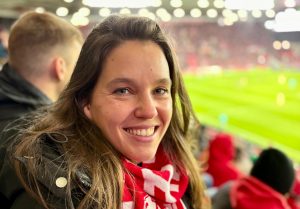 Isabell Rahms, CDU-Landtagskandidatin für Mainz, sitzt in der MEWA ARENA auf der Tribüne. Sie trägt einen rot-weißen Mainz 05 Schal und zeigt ihre Verbundenheit zur Stadt und zum Verein.