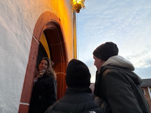 Isabell Rahms führt Gewinner der Stadtführung mit Merkurist durch den Holzturm in Mainz – einst das Gefängnis des Schinderhannes. Die Gruppe steht am historischen Eingang unter einer beleuchteten Laterne.