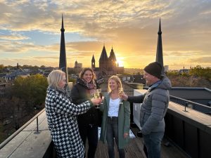 Isabell Rahms mit den Gewinnern der Stadtführung von Isabell Rahms und Merkurist über den Dächern von Mainz. Im Hintergrund der Mainzer Dom bei Sonnenuntergang – Start der Stadtführung mit Begrüßungssekt und Blick auf die Innenstadt Mainz.