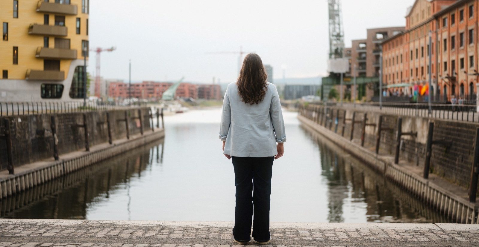 Isabell Rahms, CDU-Landtagskandidatin für Mainz, steht am Zollhafen und blickt auf das Hafenbecken. Links im Bild das goldene Gebäude Pandion DOXX, rechts das Gutenberg Digital Hub – moderne Architektur trifft Mainzer Lebensgefühl.